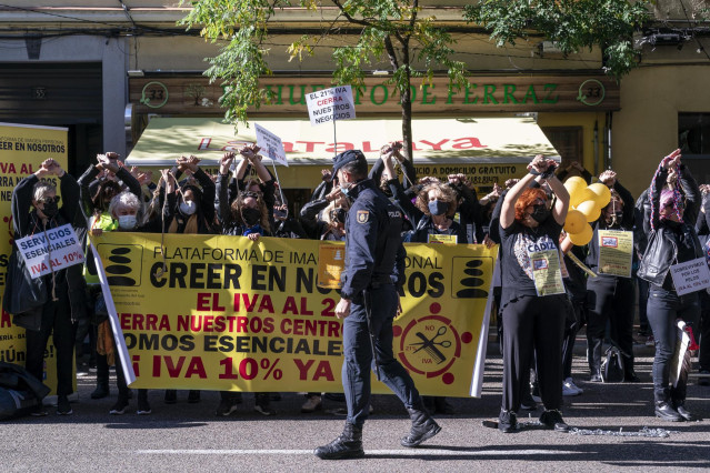 Un agente de policía supervisa a un grupo de personas perteneciente al sector de la estética durante una concentración por la bajada del IVA a la imagen personal ante la sede del PSOE