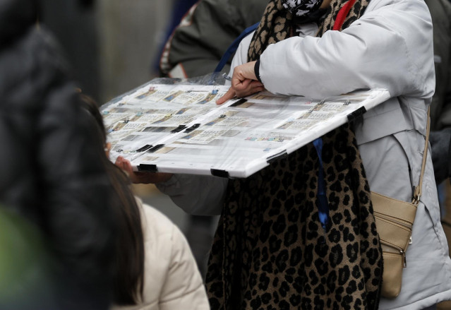 Una personas compra un décimo de lotería de Navidad a una vendedora ambulante