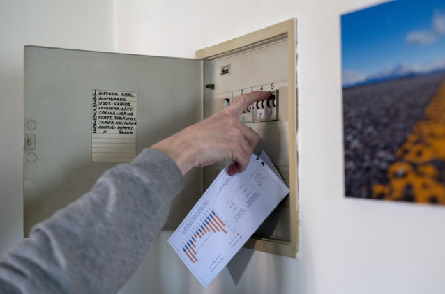 Un hombre sube los plomos de la luz con una factura de luz en la mano, a 3 de enero de 2022, en Madrid