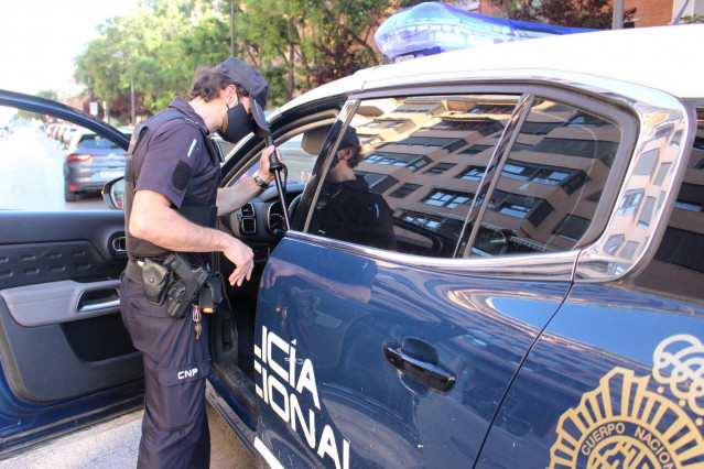 Archivo - Un agente de la Policía Nacional junto a un coche patrulla