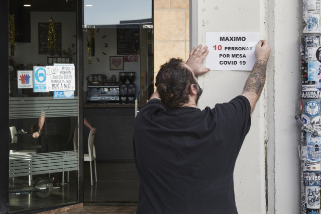 Un camarero coloca un cartel de reducción de aforo por Covid, en su bar el día en que han entrado en vigor nuevas restricciones por el coronavirus, a 29 de diciembre, en Pamplona, Navarra, (España).