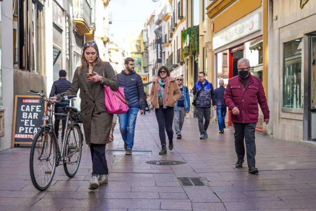 Una mujer en bicicleta y otros ciudadanos sin mascarillas y otro con  ella por la calle Sierpes, , en el primer día sin la obligación de llevar mascarillas por las calle a 10 de febrero del 2022 en Sevilla (Andalucía)