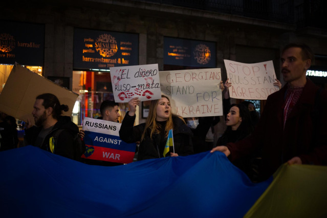 Un grupo de personas sostiene pancartas en una concentración bajando La Rambla desde la Plaza de Cataluña tras los primeros ataques rusos registrados en Ucrania