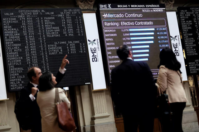 Cuatro personas frente a un panel de valores del Ibex 25 en el Palacio de la Bolsa, a 30 de mayo de 2022, en Madrid (España).