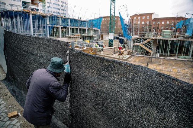 Archivo - Un hombre mira por el agujero de una lona de una obra en construcción
