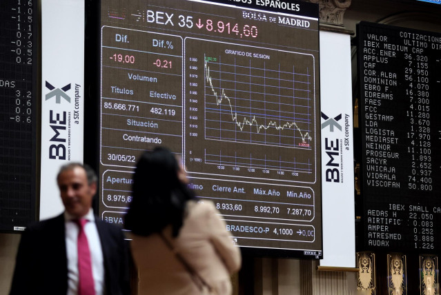 Dos personas frente a un panel de valores del Ibex 25 en el Palacio de la Bolsa, a 30 de mayo de 2022, en Madrid (España). El Ibex 35 ha retrocedido un 0,14 % en la media sesión de este lunes, hasta situarse en los 8.920, 9 puntos en una jornada marcada p