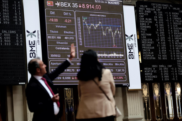 Dos personas frente a un panel de valores del Ibex 25 en el Palacio de la Bolsa, a 30 de mayo de 2022, en Madrid (España).