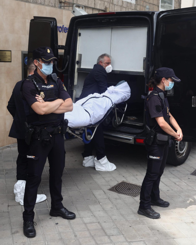 Un operario transporta el cuerpo de una de las tres personas muertas a balazos, junto a varios agentes de la Policía Nacional que custodian el portal donde han sucedido los hechos, en el número 205 de la calle Serrano, a 20 de junio de 2022, en Madrid (Es