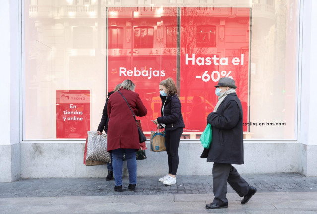 Archivo - Varias personas pasan delante de un escaparate durante las rebajas de enero