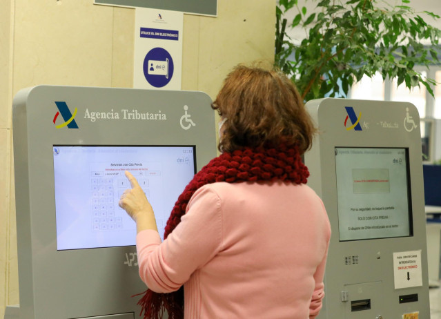 Archivo - Una mujer recoge su turno en una oficina de la Agencia Tributaria.