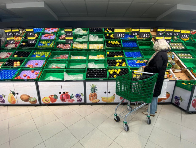 Archivo - Un mujer coloca fruta en una bolsa mientras observar los productos que quedan en las cajas de un supermercado