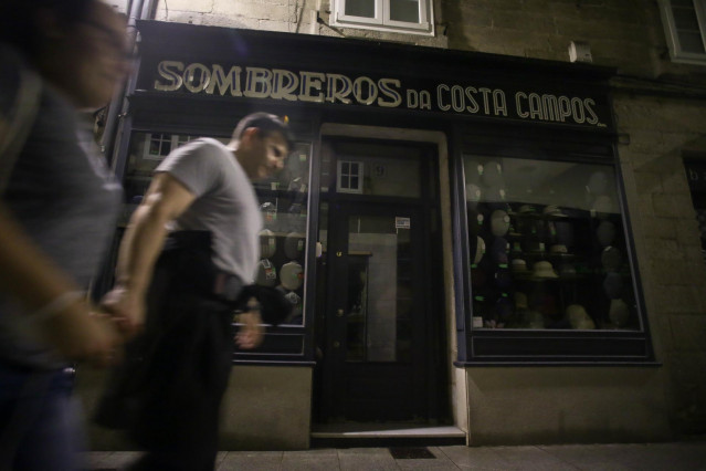 Varias personas caminan al lado de una tienda de ropa sin iluminación, a 10 de agosto de 2022, en Lugo, Galicia (España).