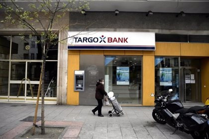 Una mujer protegida con mascarilla pasa delante de una oficina Targobank. -