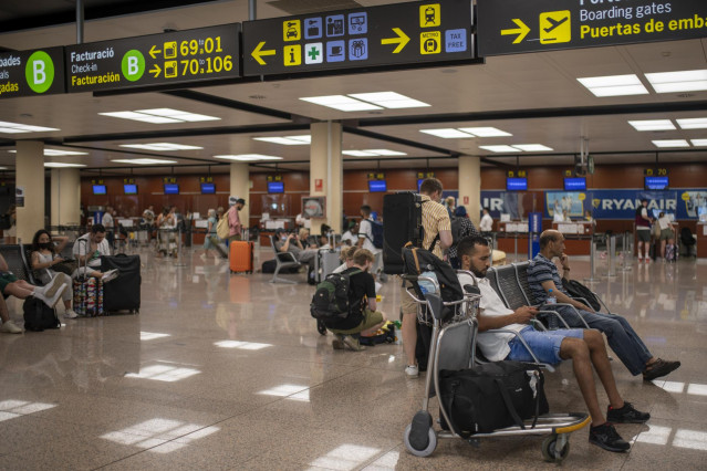 Archivo - Varias personas esperan sentadas con sus maletas en el Aeropuerto Josep Tarradellas Barcelona-El Prat, a 8 de agosto de 2022, en Barcelona, Catalunya (España).