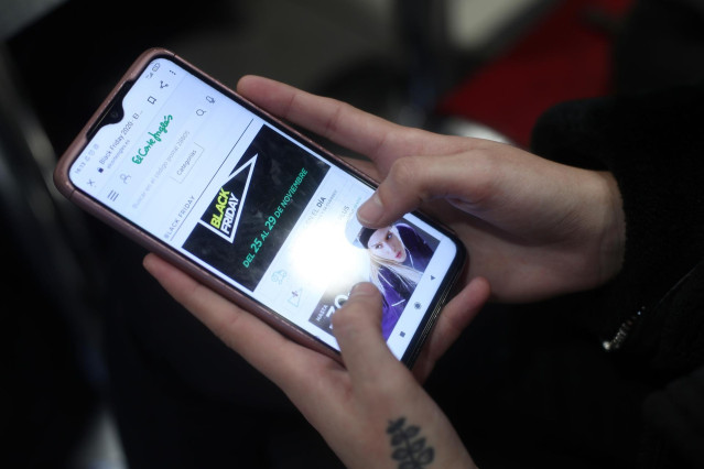 Archivo - Una joven consulta las ofertas de Black Friday de un comercio en su móvil