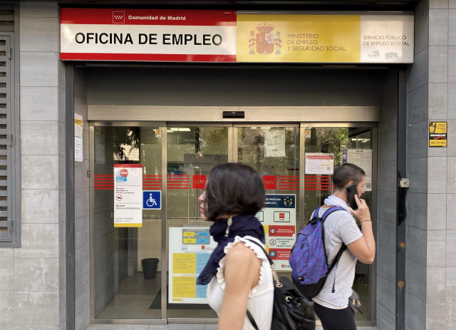 Archivo - Dos jóvenes pasando por delante de una oficina de empleo