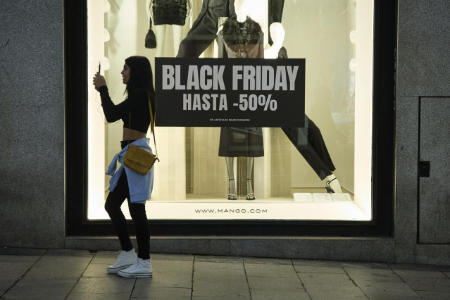 Varias personas pasan por delante de los comercios que anuncian los descuentos del Black Friday