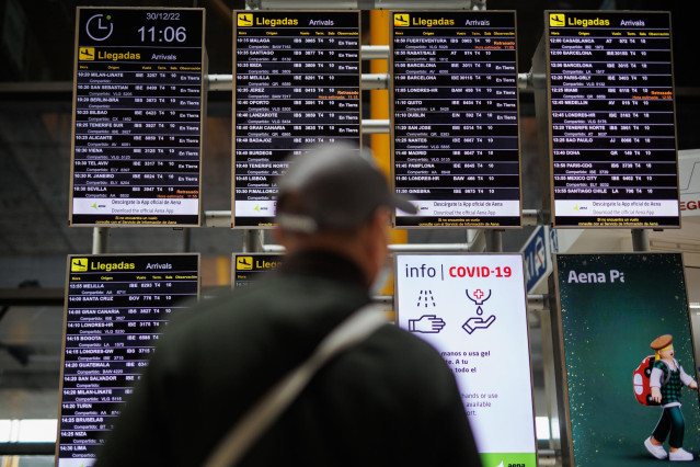 Un hombre con mascarilla observa los paneles informativos de las salidas de los vuelos en el aeropuerto Adolfo Suárez Madrid-Barajas, a 30 de diciembre de 2022, en Madrid (España).