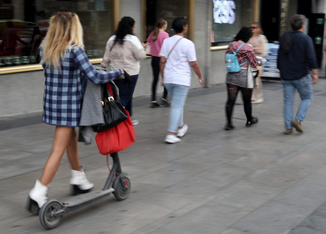 Archivo - Una mujer camina con un patinete eléctrico, a 3 de octubre de 2022, en Madrid (España).