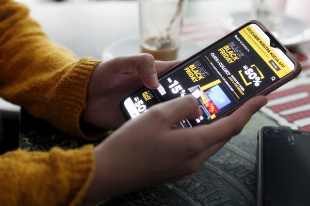 Archivo - Una joven consulta las ofertas de Black Friday de un comercio en su móvil