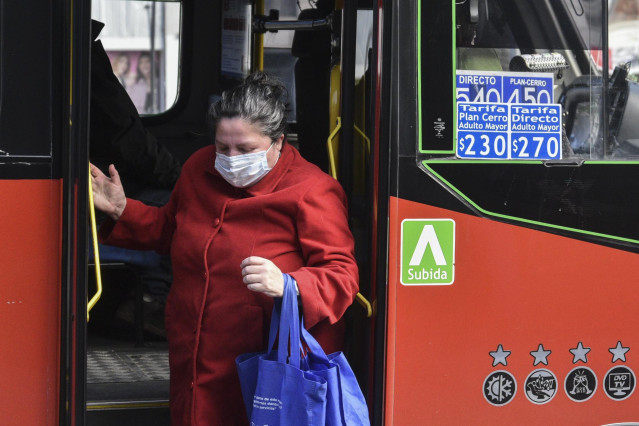 Archivo - Una mujer con mascarilla baja de un autobús en Chile