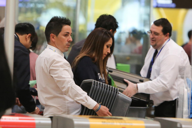 Archivo - Un trabajador del Aeropuerto Adolfo Suárez Madrid- Barajas, mueve las cajas del control de suguridad del aeropuerto.