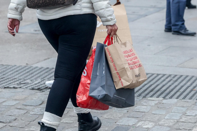 Archivo - Una persona camina con varias bolsas de compras por una calle comercial de Madrid.