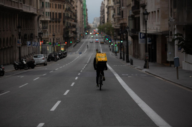 Archivo - Un trabajador de Glovo en bicicleta por una calle de Barcelona, prácticamente vacía durante el confinamiento por la pandemia.