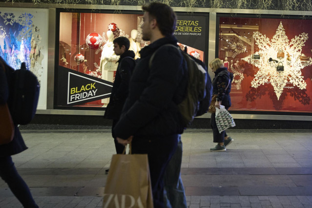 Archivo - Varias personas pasan por delante de los comercios que anuncian los descuentos del Black Friday