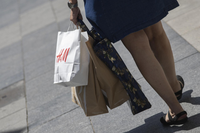 Archivo - Una mujer pasea cargada con varias bolsas, una de ellas perteneciente a la tienda H&M, durante el segundo día de rebajas, en Madrid (España), a 26 de junio de 2020.