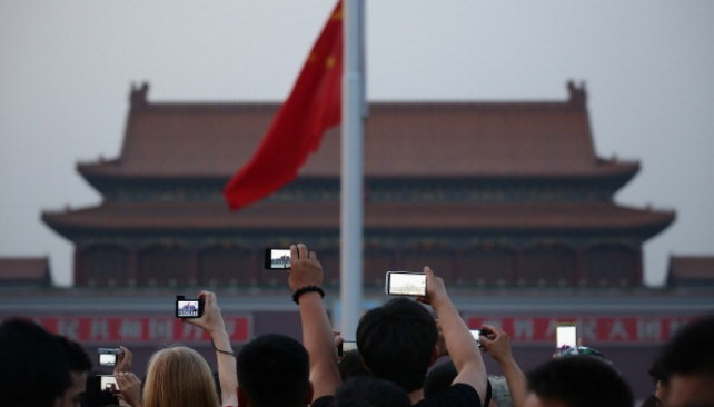 Archivo - Chinese tourists watch the customary ceremony of lowering flag at Tiananmen Square on June 3, 2013 in Beijing, China.