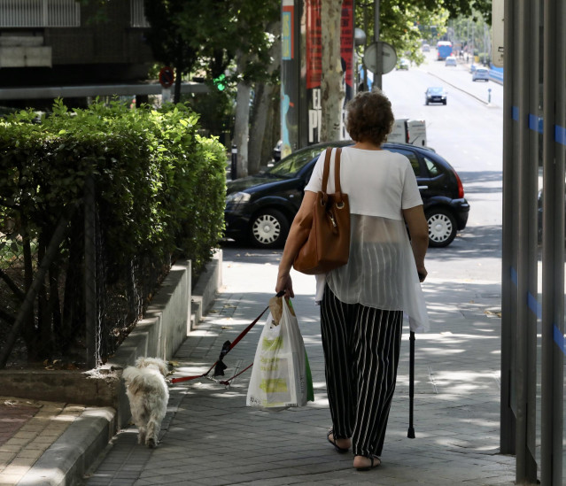 Archivo - Una mujer de la tercera edad pasea con su perro por una calle de Madrid (26 de julio de 2019).
