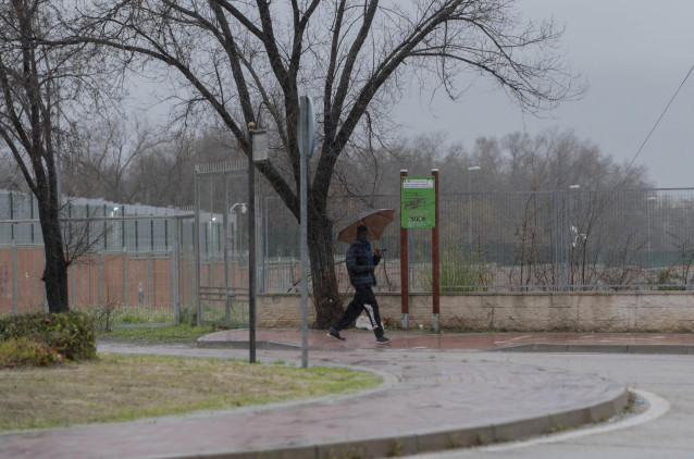 Un migrante se protege de la lluvia con un paraguas en las inmediaciones del centro de Emergencia, Acogida y Derivación en el Acuartelamiento 'Primo de Rivera'en Alcalá de Henares.
