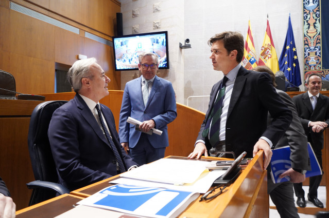 El presidente del Gobierno de Aragón, Jorge Azcón, conversa con los diputados del PP Ramón Celma y Joaquín Juste antes de la sesión plenaria de las Cortes autonómicas.