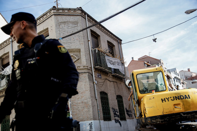 Archivo - Un agente de Policía Nacional frente a una máquina retroexcavadora durante la demolición del edificio okupado ‘La Higuera’, en el barrio de Tetuán, Madrid