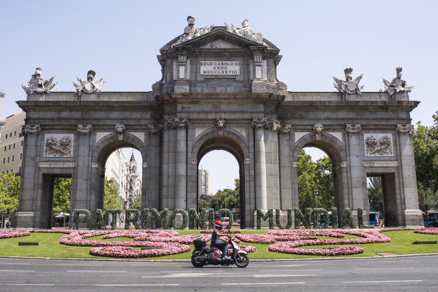 Archivo - Una moto pasa por las letras gigantes que forman la palabra ‘Patrimonio Mundial’ en la Puerta de Alcalá