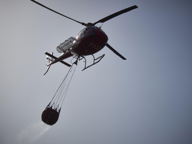 Archivo - Un helicóptero lanza agua para sofocar un incendio