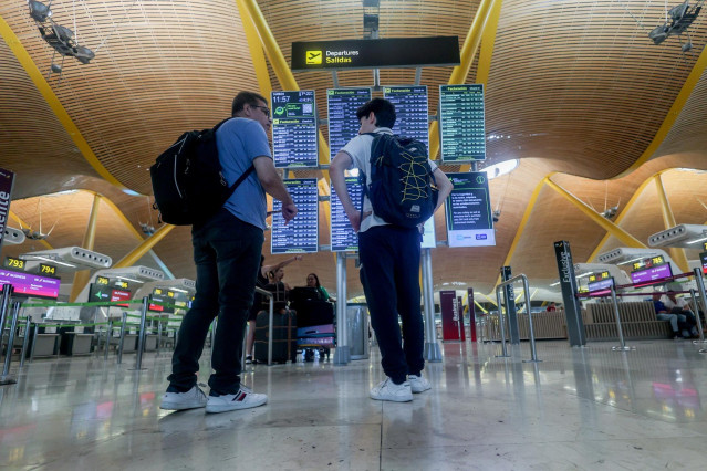 Dos personas observan el panel de salidas con motivo de la operación salida del puente de agosto, en la T4, en el aeropuerto Adolfo Suárez Madrid-Barajas, a 14 de agosto de 2024, en Madrid (España).
