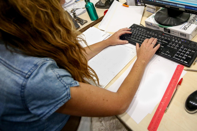 Archivo - Una mujer escribe en el teclado de su ordenador, con papeles alrededor mientras trabaja en la oficina.
