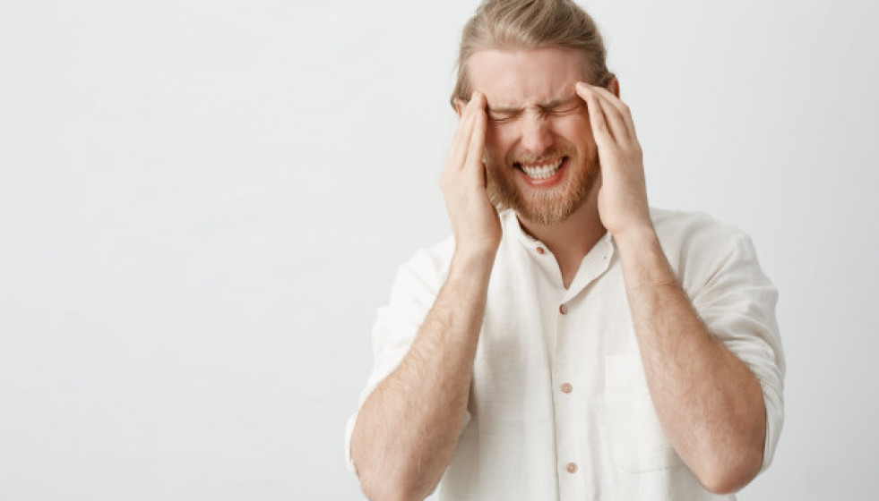 Indoorportraitcaucasianblondmanwithbeardsufferingfrommigraineheadacheholdingfingerstemples