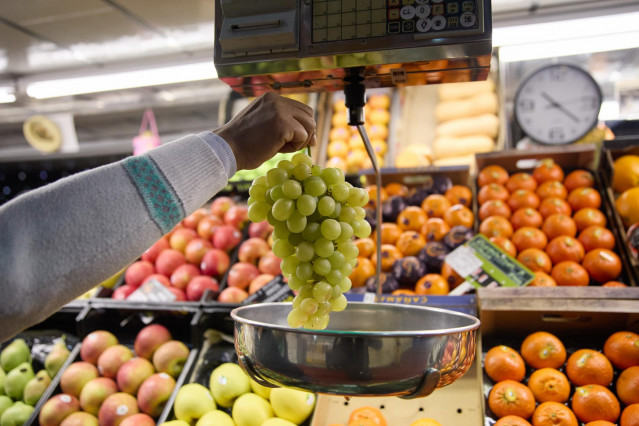 Archivo - Un dependiente pesa un racimo de uvas en un mercado