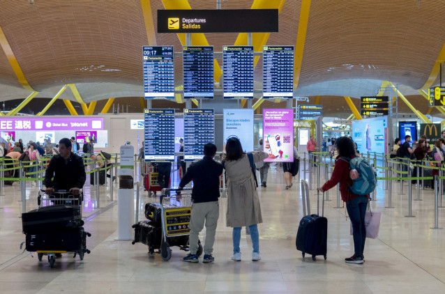 Archivo - Un grupo de personas frente al panel del orden de vuelos en la terminal T4 del aeropuerto de Adolfo Suárez-Madrid Barajas, en Madrid (España).