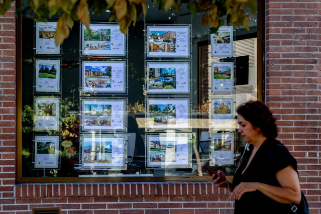 Archivo - Una mujer camina frente a un escaparate de anuncios de viviendas, a 4 de agosto de 2023, en Madrid (España).