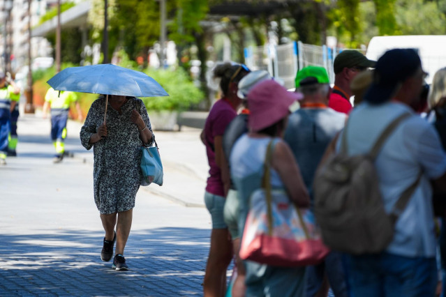 Una mujer con una sombrilla junto a un grupo de turistas.