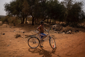 Archivo - Un niño con una bicicleta en un camino de la aldea de Ganguel, en Níger