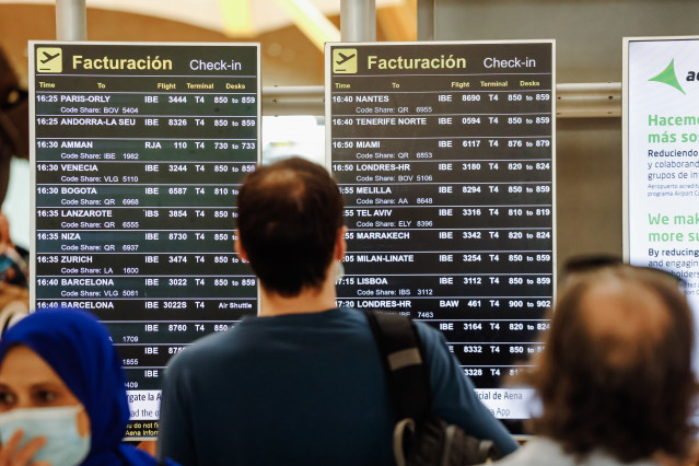 Archivo - Pasajeros observan las pantallas con los vuelos de la Terminal 4 del Aeropuerto Adolfo Suárez Madrid.