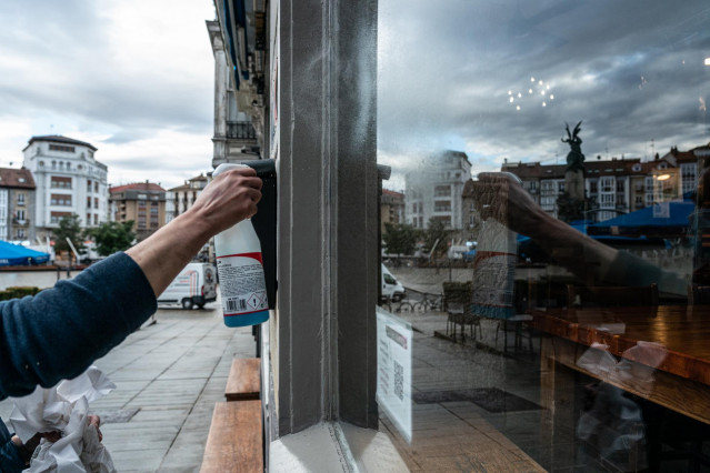 Archivo - Una camarera limpia el cristal de su cafetería