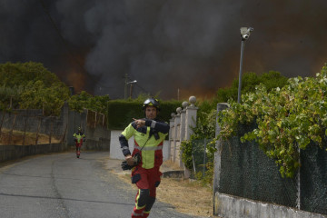Dos bomberos colaboran en la extinción del incendio, a 12 de agosto de 2025, en Seixalbo, Ourense, Galicia (España).