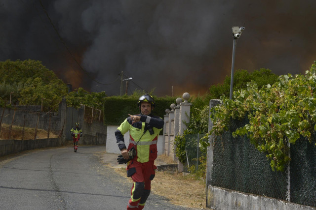 Dos bomberos colaboran en la extinción del incendio, a 12 de agosto de 2025, en Seixalbo, Ourense, Galicia (España).