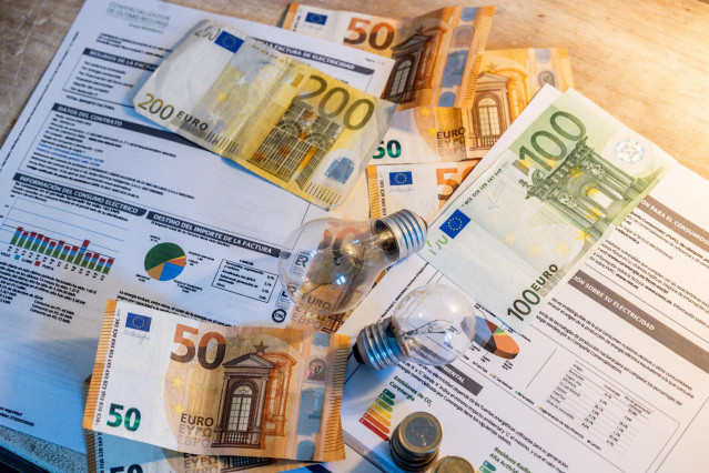Archivo - Dos bombillas sobre billetes, monedas y facturas, a 9 de enero de 2025, en Madrid (España).